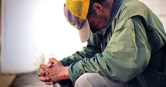 homeless man on the street with head down