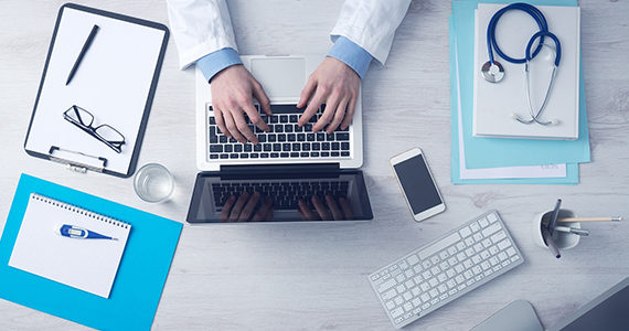 Doctor typing on laptop with other equipment on desk