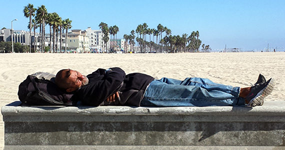 Homeless man lying down on concrete slab on Venice beach
