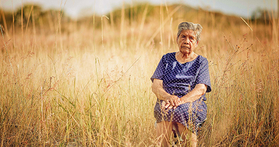 Older Latino woman sits in a field