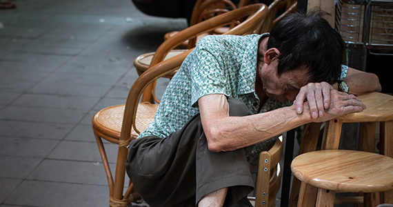 Older Chinese man leaning over stool with head down