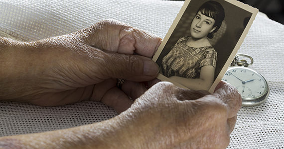 Older woman holding old photo of herself when she was young