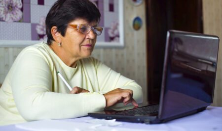 Senior old woman in eyeglasses surfing internet on laptop at home